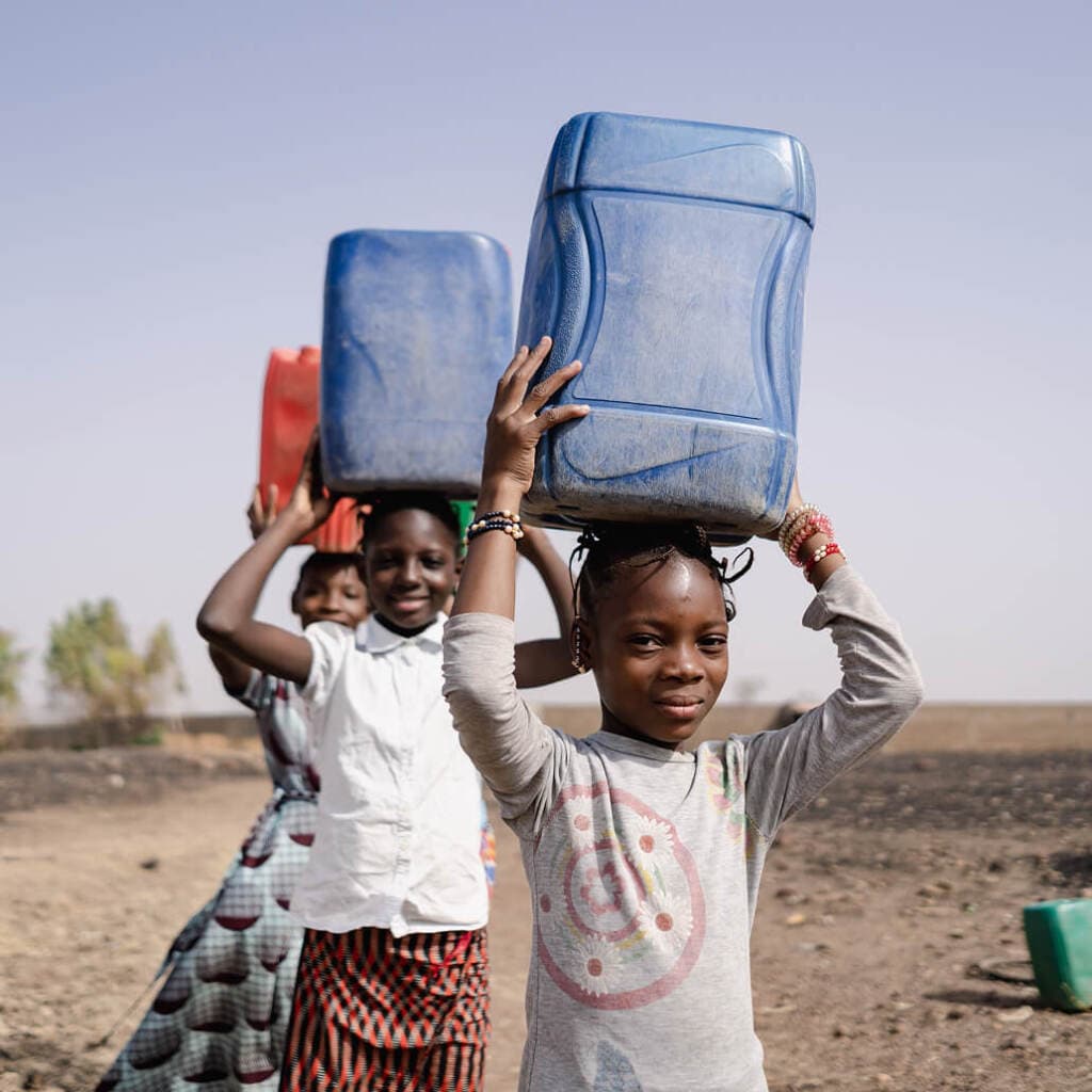 Girls transport water in plastic containers, highlighting rural water access challenges.